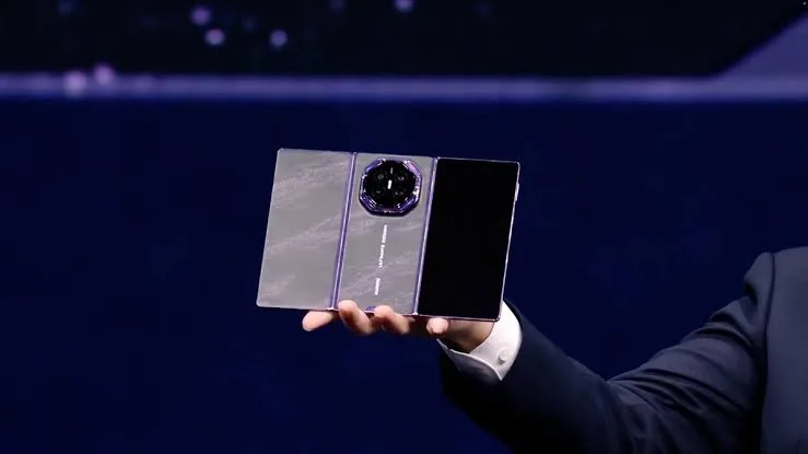 A three-panel Huawei folding phone held up on stage during a launch event
